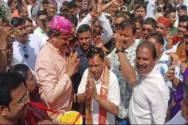 भीड़ के बीच हाथ जोड़कर खड़े जगदीश देवड़ा और गुलाबी साफा पहने एक व्यक्ति, आसपास मौजूद लोग फूल बरसा रहे हैं