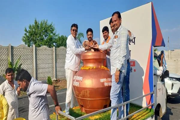 सजे हुए वाहन पर रखे बड़े कलश के पास खड़े पुरुष और उसके भीतर हाथ डालते कुछ लोग